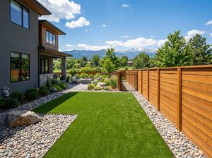 Side-yard artificial turf dog run with river-rock borders alongside a modern Colorado home, snow-capped peak in the distance