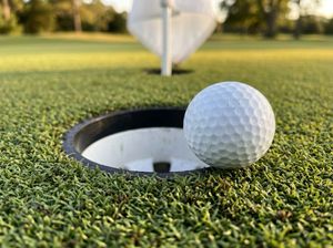 Close-up of a golf ball at the lip of a regulation cup on a tour-grade nylon putting surface
