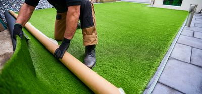 Installer rolling artificial turf into place beside a patio
