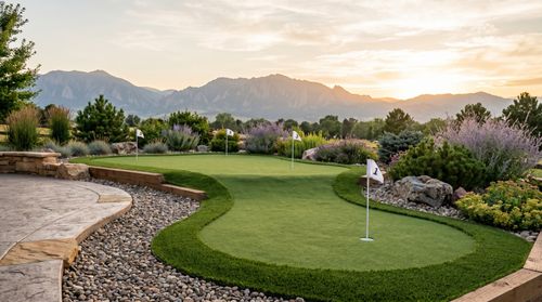 Multi-tier backyard artificial putting green with three pin flags at golden hour, Denver foothills in background